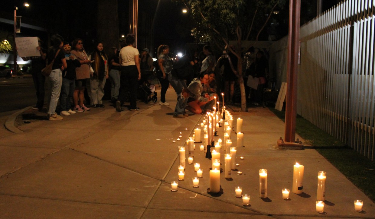 dozens of candles burn on a sidewalk
