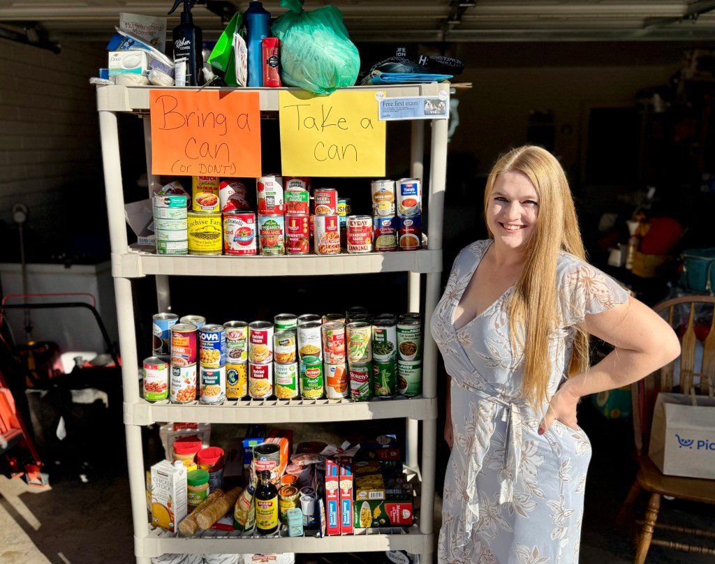 A woman stands next to a shelf of canned goods.