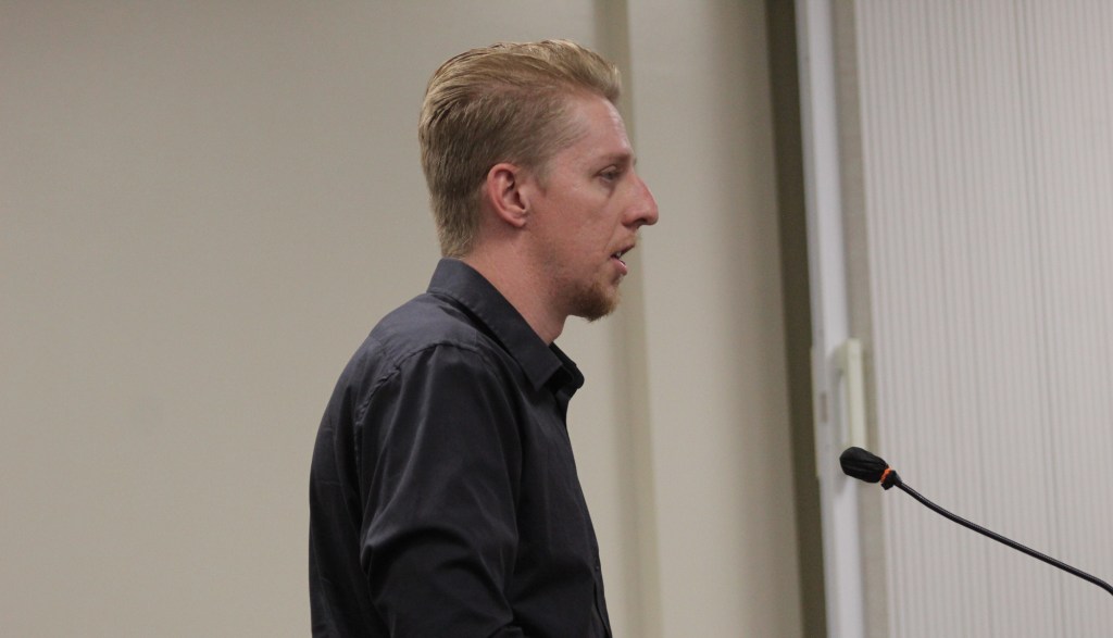 a thin man stands at a microphone