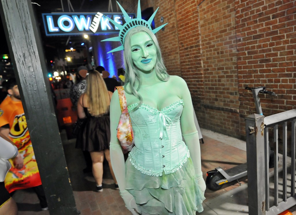 A woman dressed in a Statue of Liberty costume outside a bar.