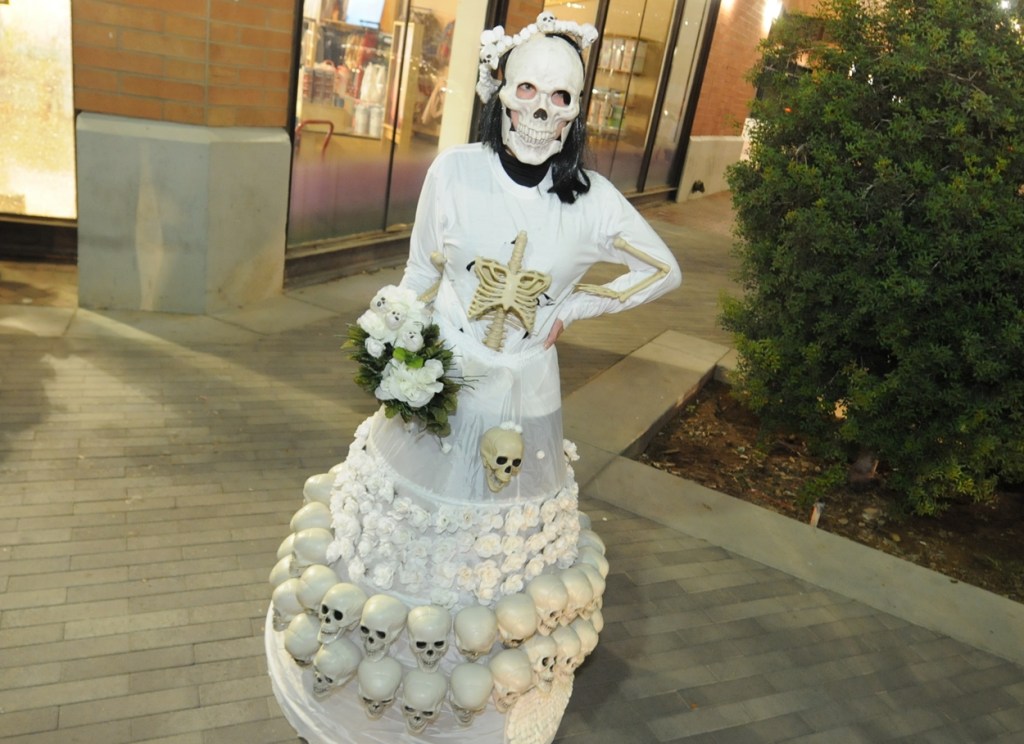 A masked woman in a skeleton-inspired white dress outside a store.