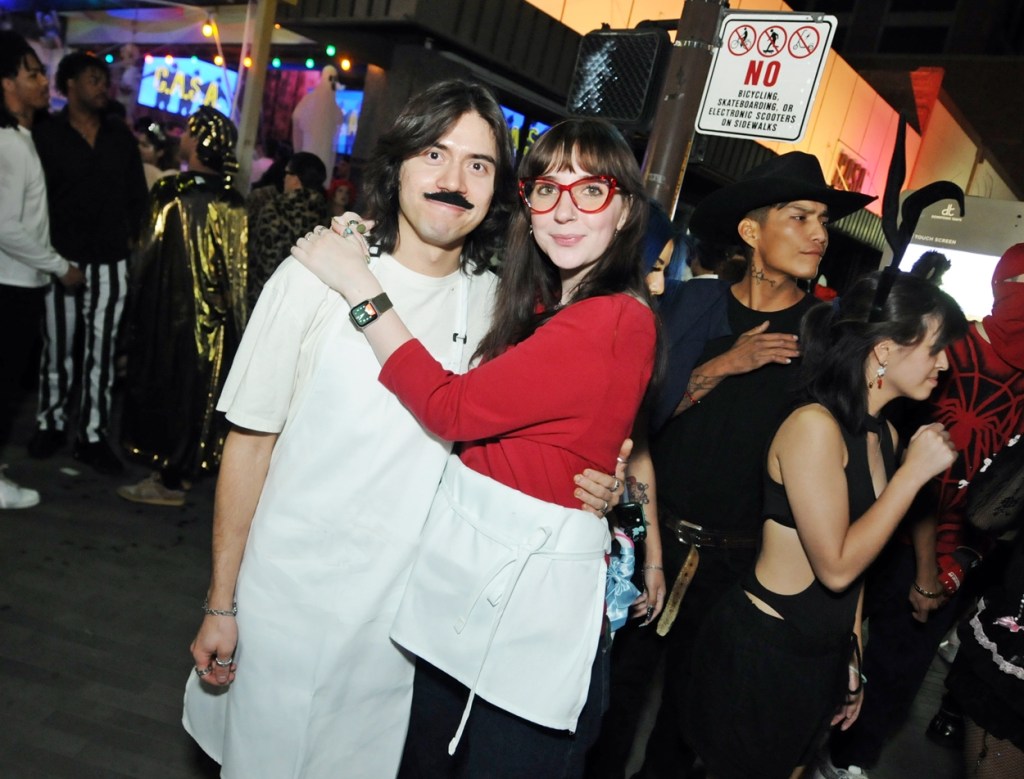 A man and woman dressed as Bob and Linda Belcher from "Bob's Burgers" on a crowded sidewalk at night.