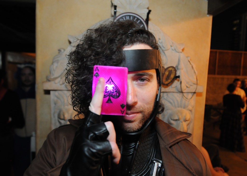 A man dressed as Gambit from The X-Men holding a glowing card in front of his face.