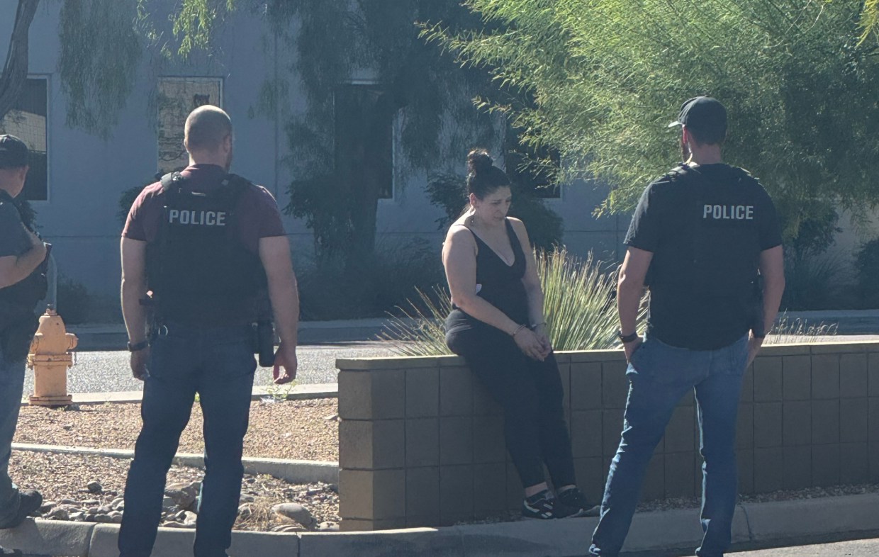 police surround a woman sitting on a low block wall