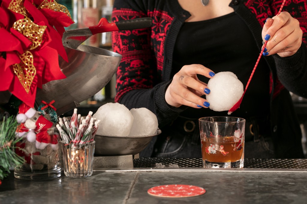 Bartender adding a large ice cube to a rocks glass.