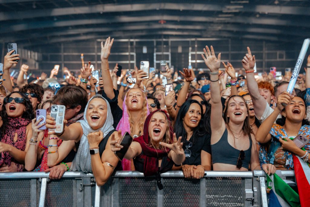A huge crowd of people stand behind a security barrier at a music festival.