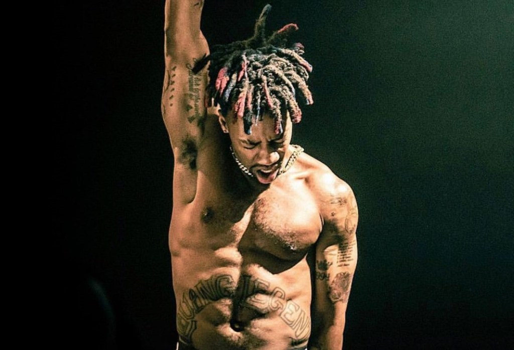 A muscular black man with his shirt off and right arm raised.