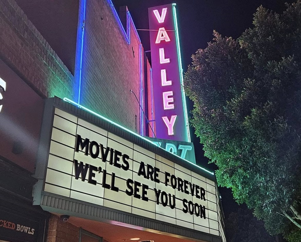 The marquee of a neon-lighted historic movie theater that says, "Movies are forever. We'll see you soon."