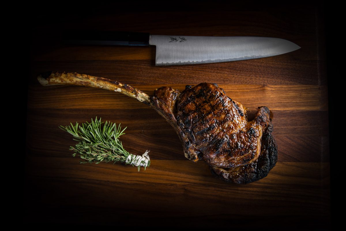 A steak on a cutting board with a knife.