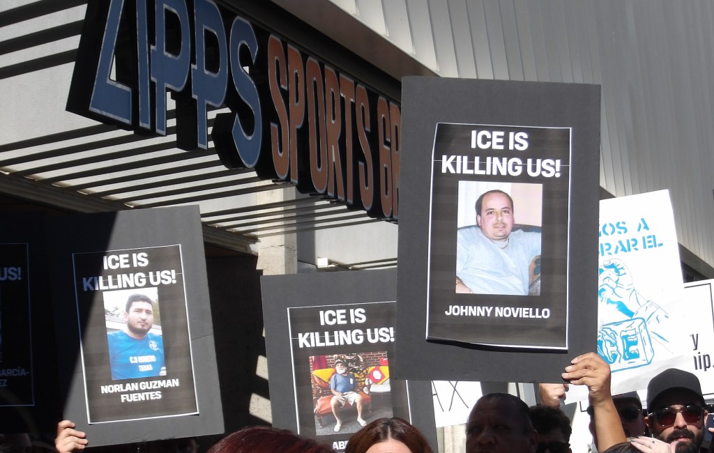 activists hold up signs of people killed in ICE custody