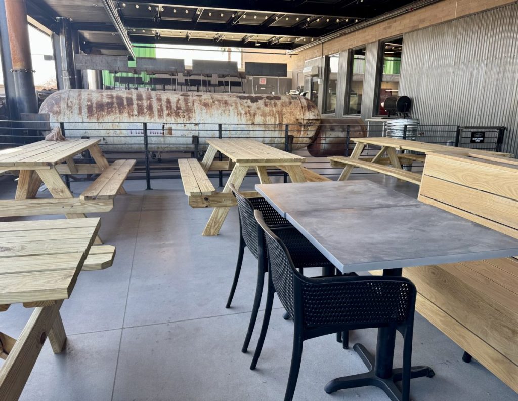 A barbecue restaurant patio, with a view of large drum smokers.