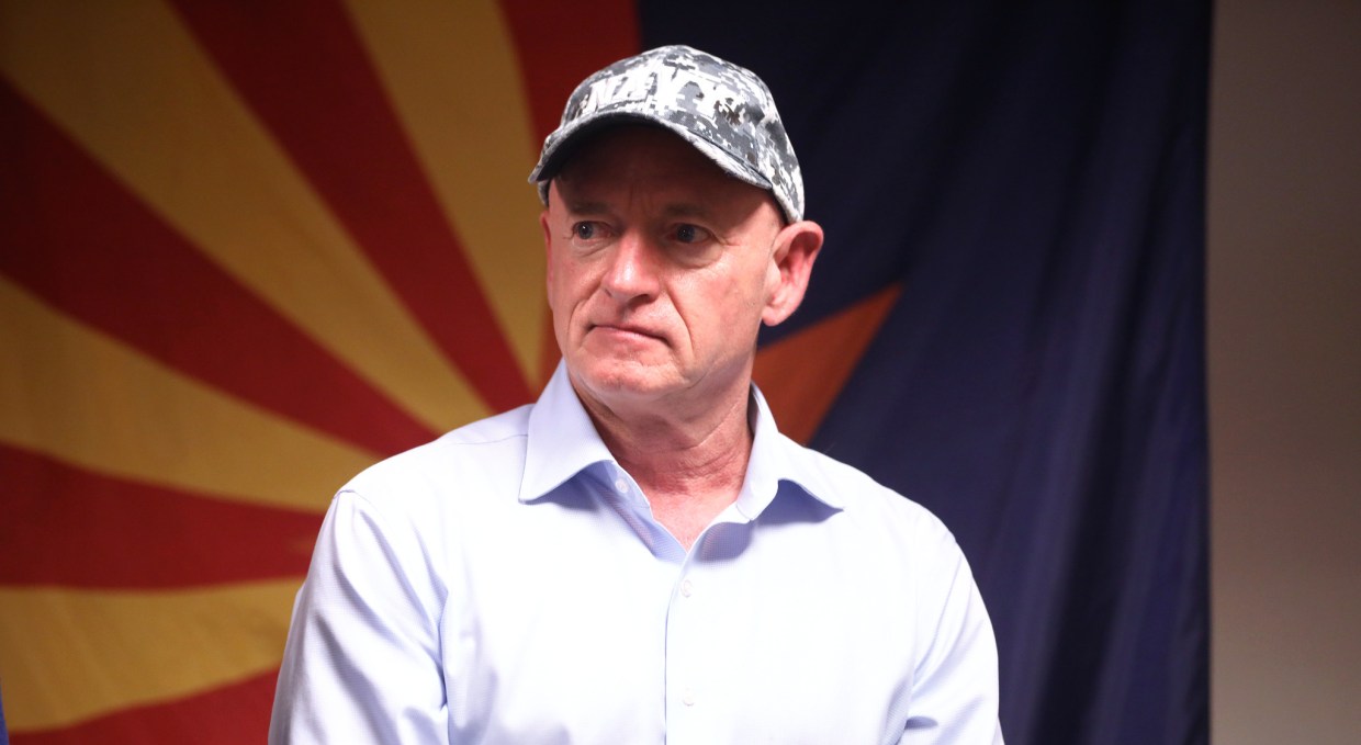 mark kelly in a hat before an arizona flag backdrop