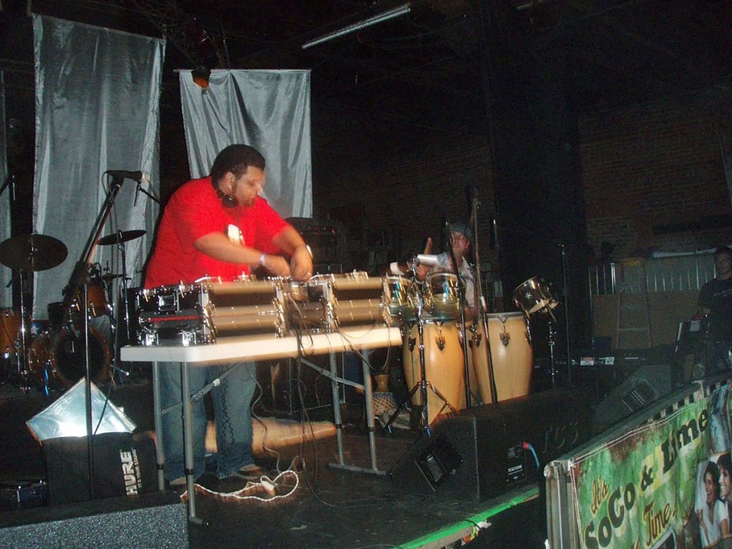 A Cuban man in a red shirt DJs on a stage.