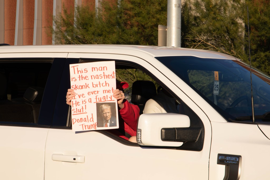someone holds an anti-trump sign out of a car window