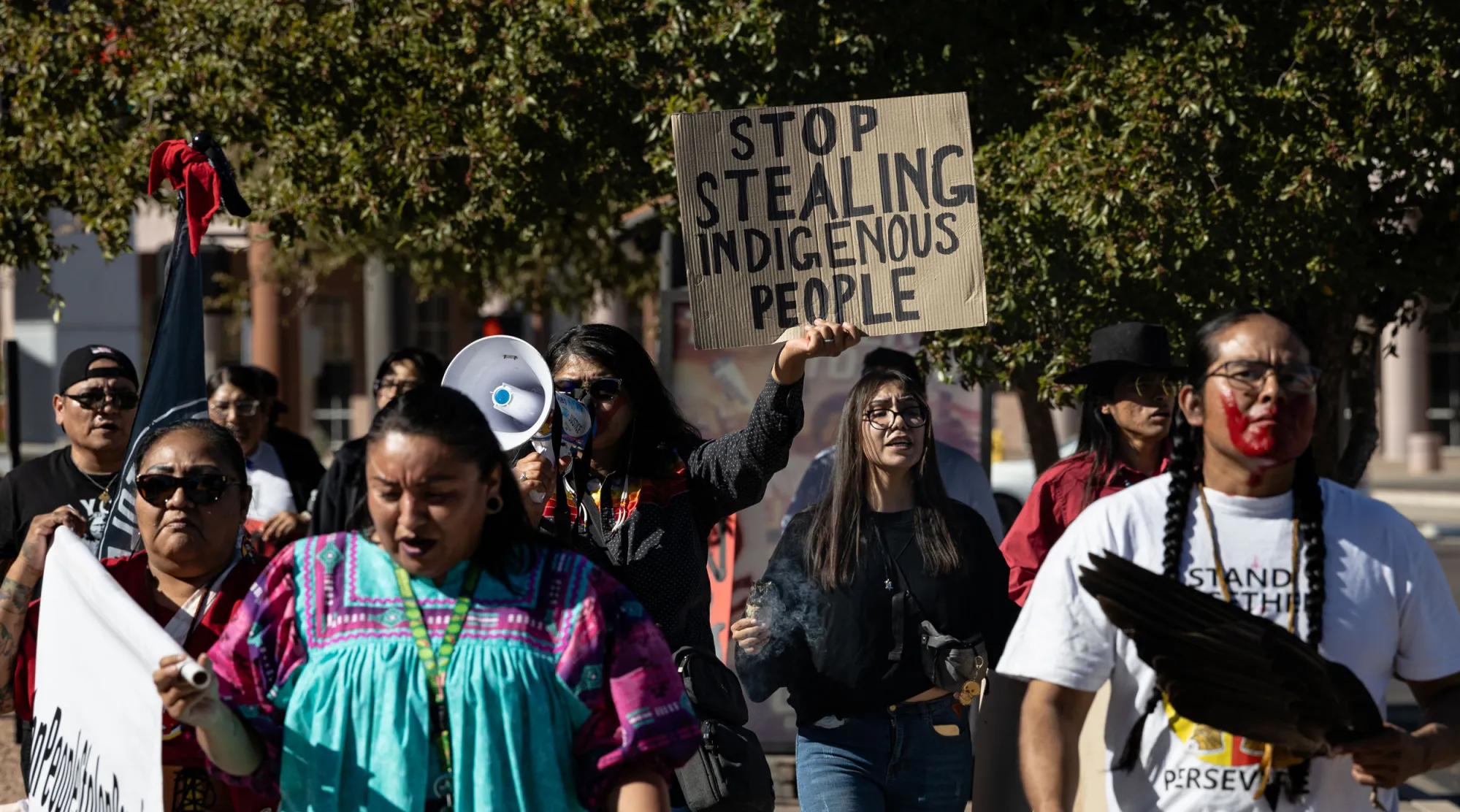 indigenous protesters march. one holds a sign that says "stop stealing indigenous people"