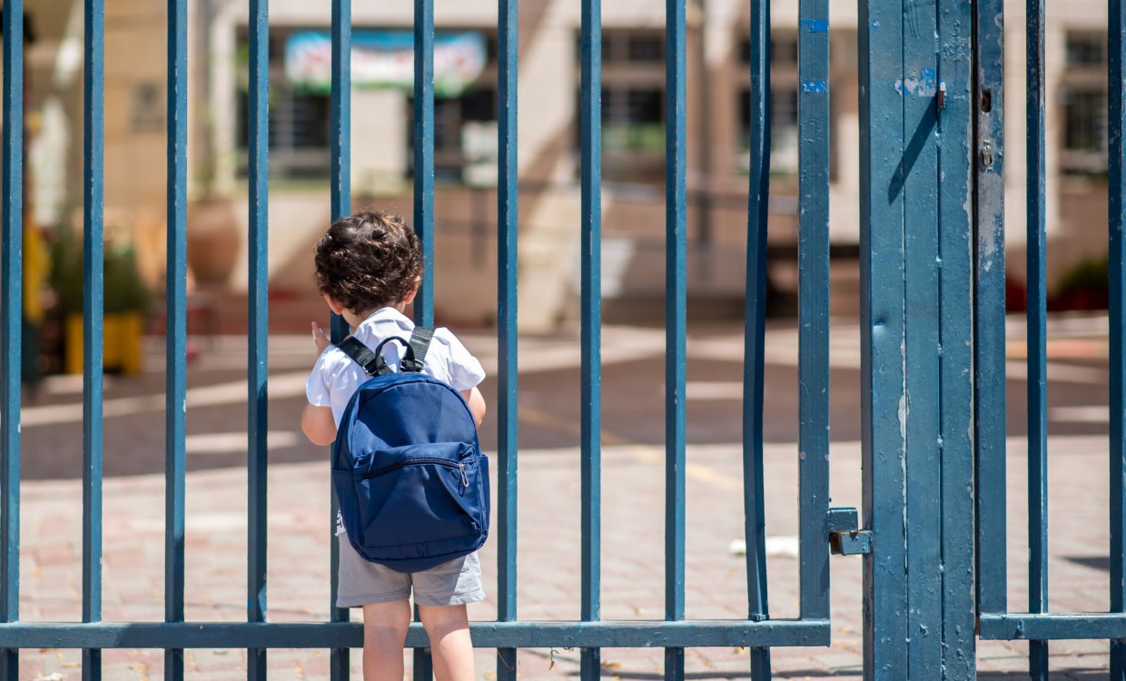 a small child wearing a backpack looks through a metal school gate