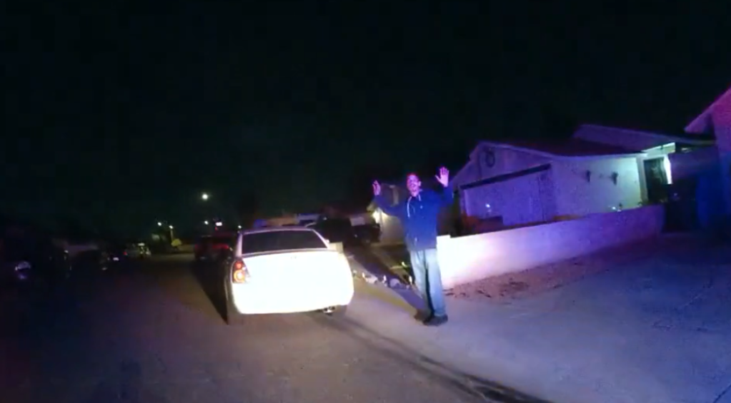 body cam footage of a light shining on a thin man with his hands in the air. it is nighttime.