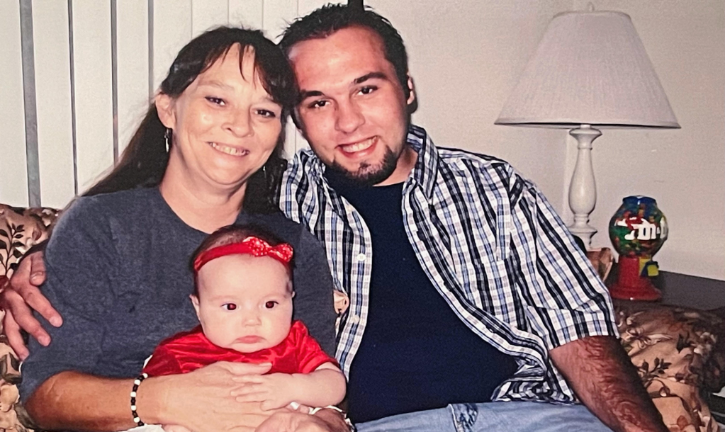 a woman holds a baby next to a young man