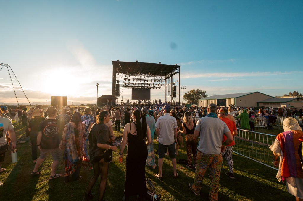 people stand in a field watching a band on a large outdoor stage