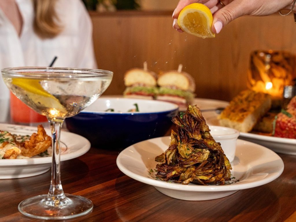 A person squeezing a lemon wedge over a plate of baby artichokes
