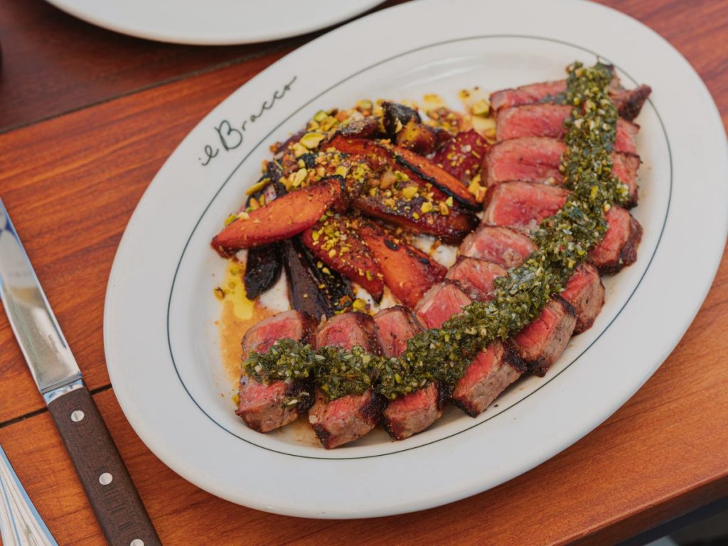 A skirt steak on a platter with salsa verde and roasted vegetables.