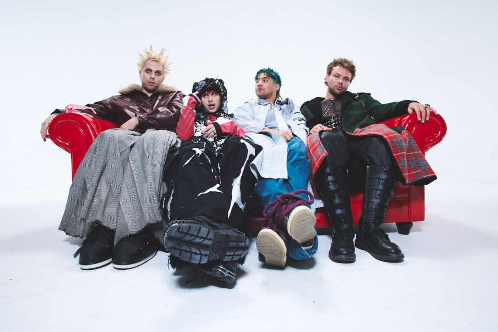 5 Seconds of Summer band members sitting on a red couch in a promotional photo for their 2026 tour.