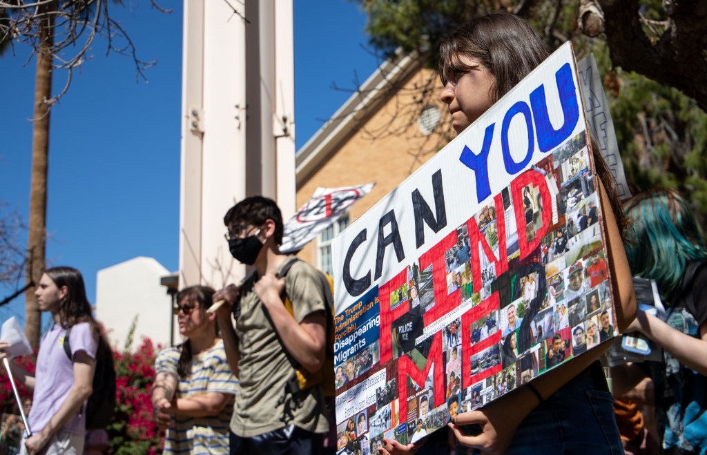 a protester holds a sign that says "can you find me" with pictures of people detained by ICE