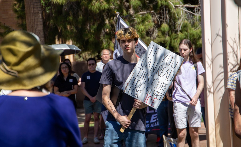a protester holds a sign that says "if you can read this, you're too smart for ICE"
