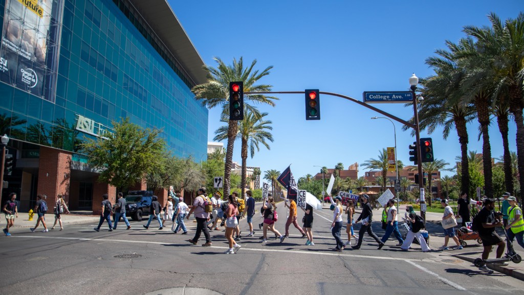 protesters walk across college ave on a sunny day in tempe