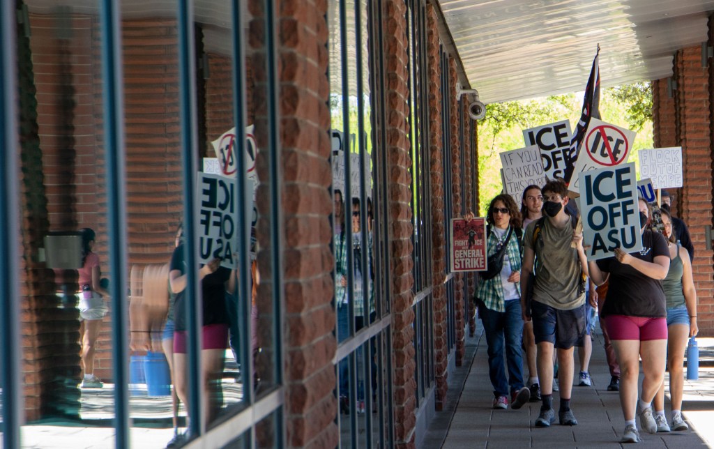 protesters walk next a building holding anti-ice signs