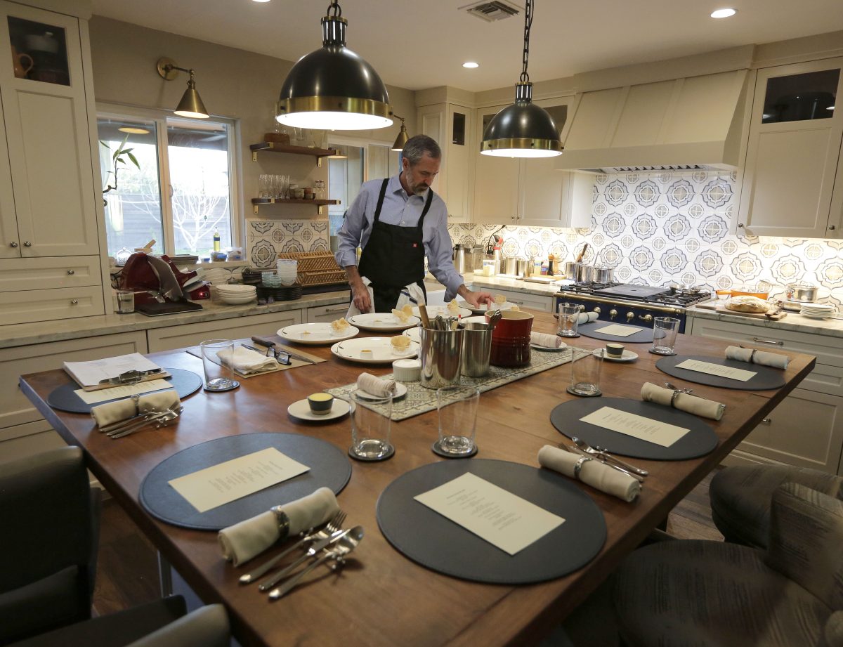 Chef Kevin Binkley stands in his home kitchen before a kitchen island with place settings.