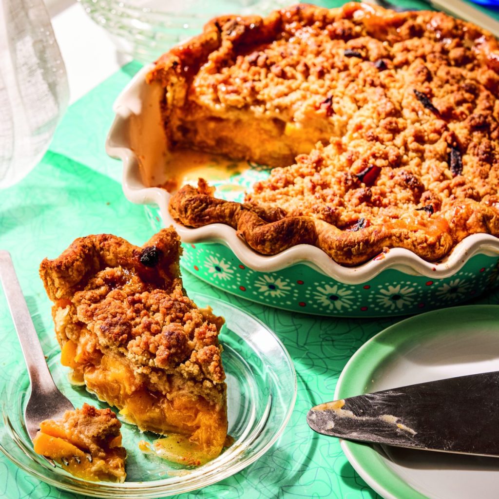 A slice of peach pie next to the entire pie in a colorful green baking dish.