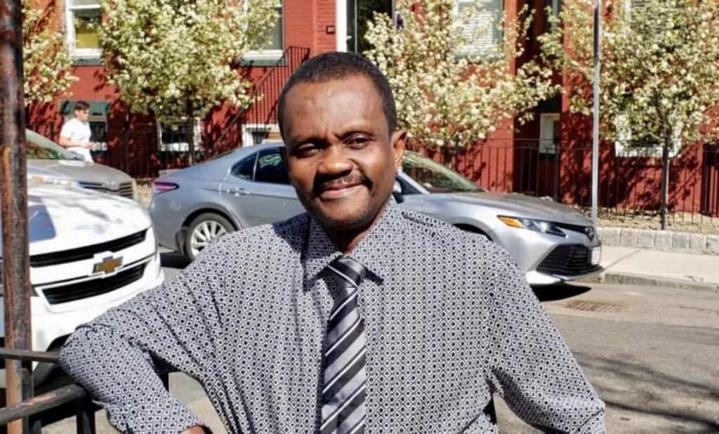 Emmanuel Damas in a gray shirt and tie on a city street