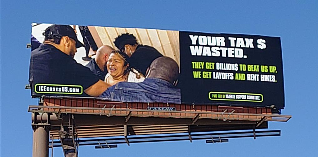 a billboard showing a swarm of ICE agents arresting a woman. it says "Your Tax $ Wasted. They get billions to beat us up. we get layoffs and rent hikes."