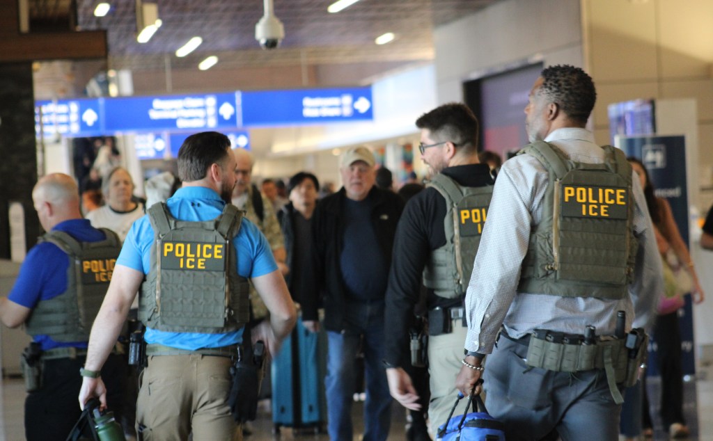 men in "police: ICE" vests walk through sky harbor airport