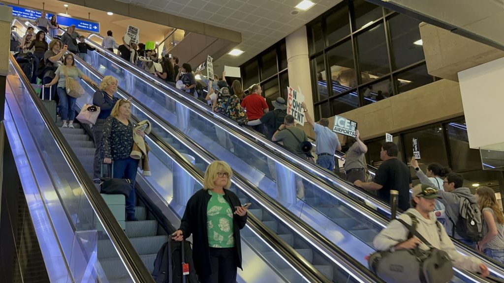 anti-ice protesters wave signs as the ride an escalator up at an airport