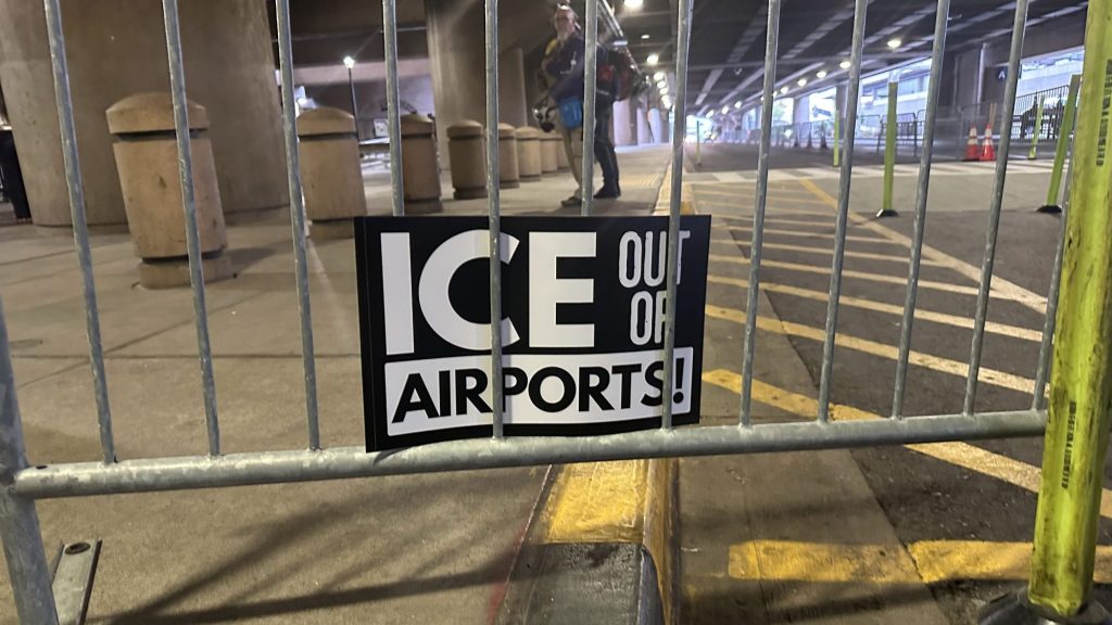 an "ice out of airports" sign stuck to a metal barrier