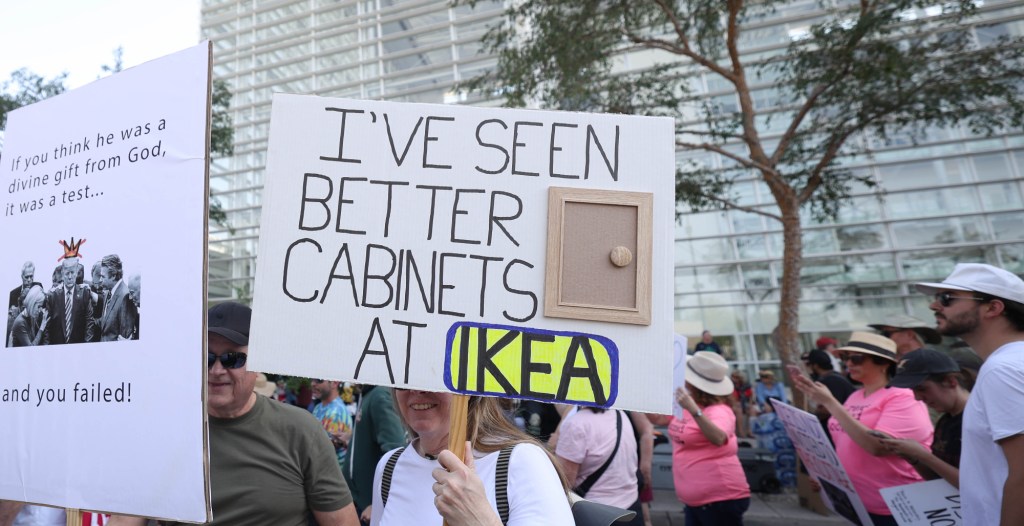a protester holds a sign with a cabinet door that says "i've seen better cabinets at ikea"