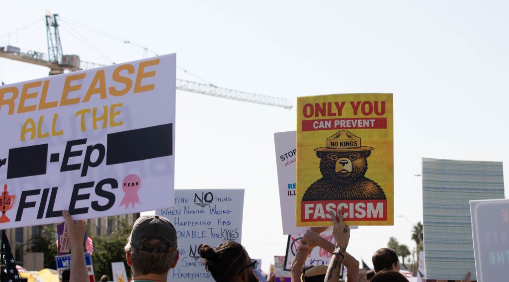 a protester holds up a sign with smokey the bear that says "only you can stop fascism"
