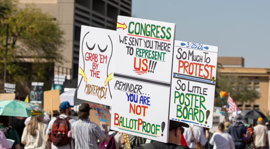 a protester holds up several signs, one of which has an outline of a naked woman -- a reference to a note donald trump once sent jeffrey epstein -- that says "grab em by the midterms"