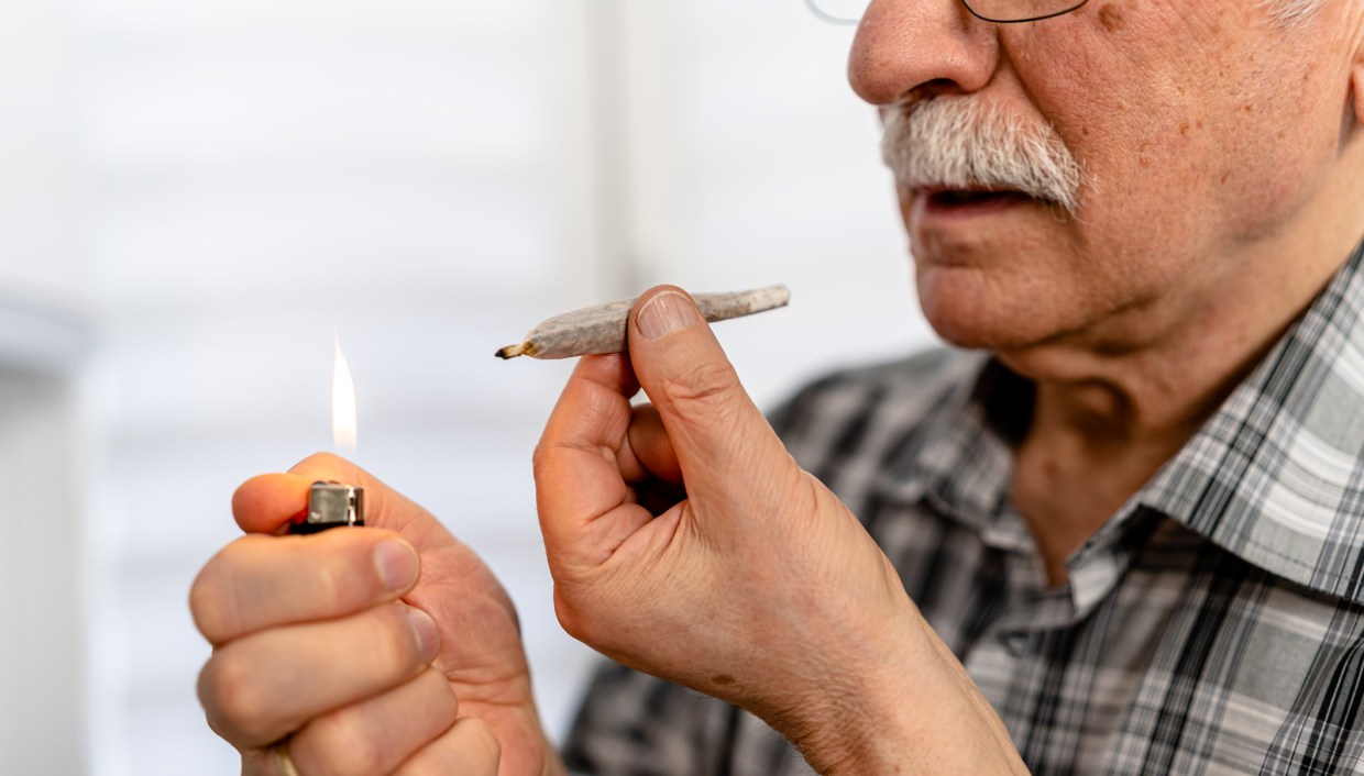 an older man with a white mustache prepares to light a weed preroll