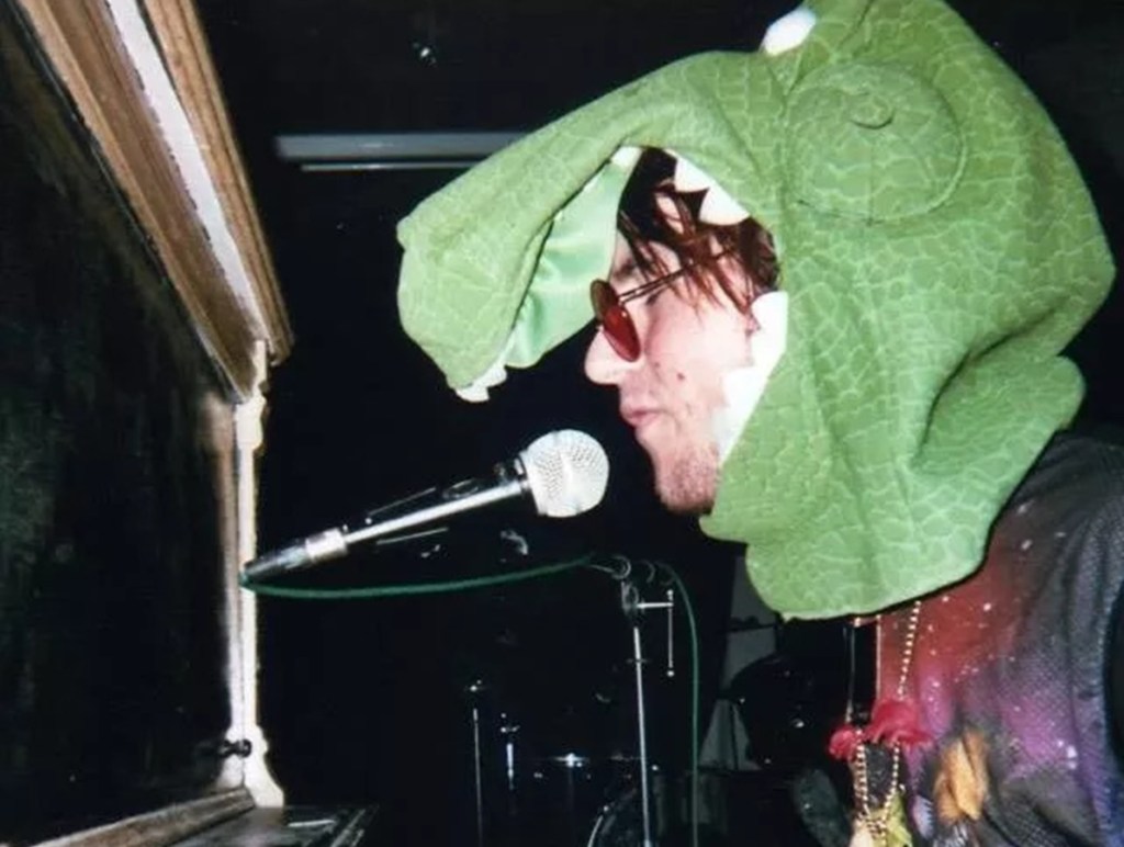 Phoenix indie musician Dinosaur Love singing into a microphone while wearing a T-Rex mask.
