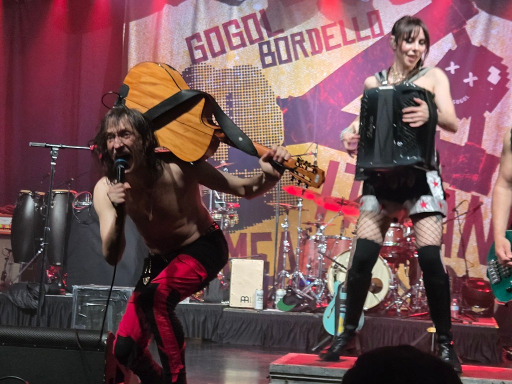 Eugene Hütz screams with a guitar resting on his shoulder during a Gogol Bordello set