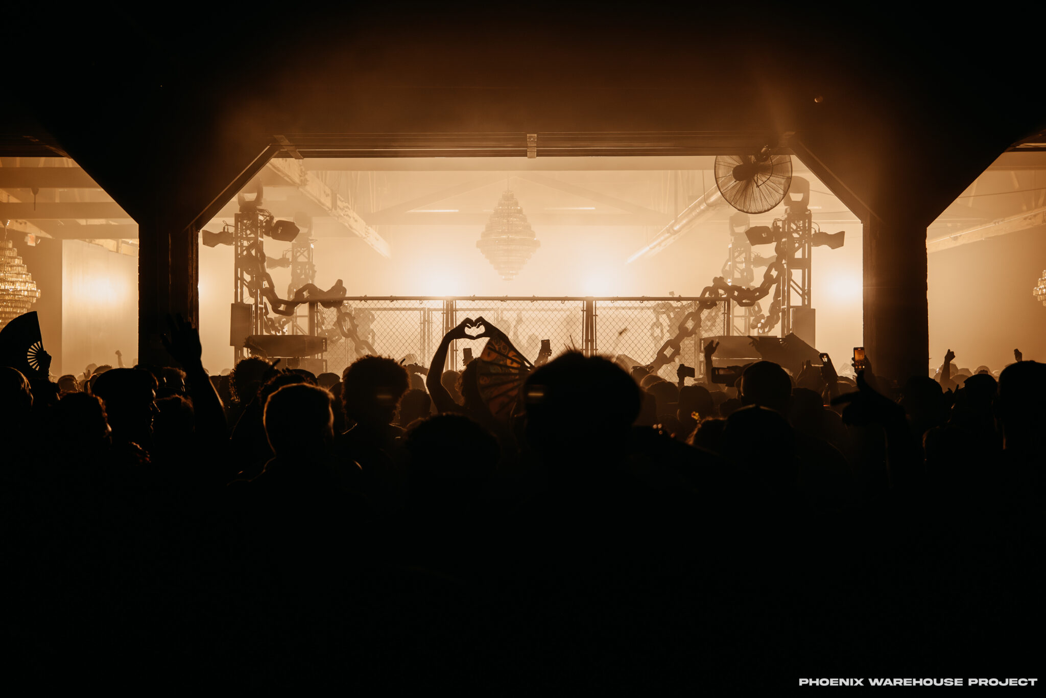 A crowd of EDM fans gathered for a concert inside a warehouse space.