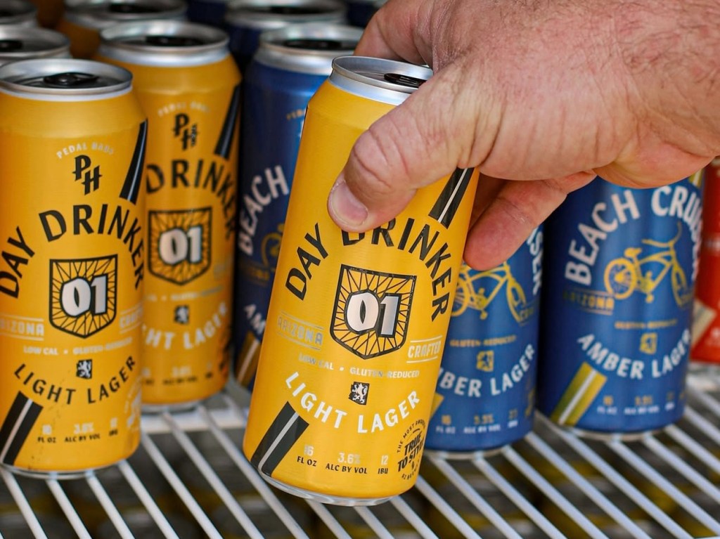 A man's hand grabs a Day Drinker Light Lager from a beer fridge.