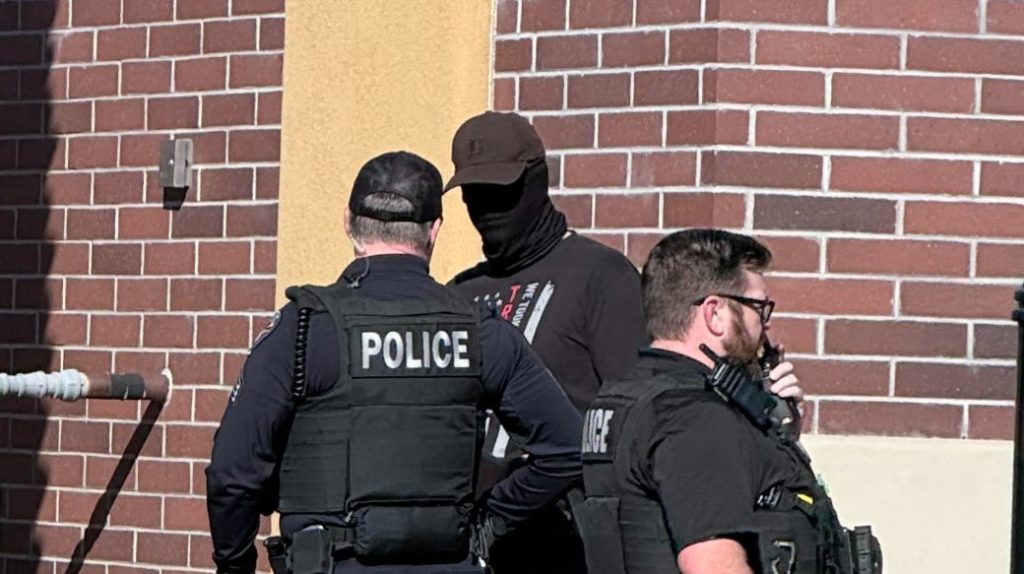 two police officers speak to a masked man near a building