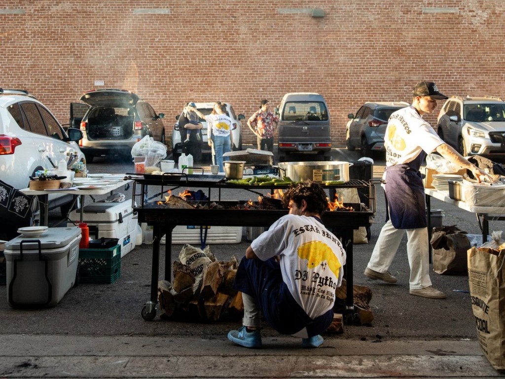 A chef tends to a grill while another prepares plates.