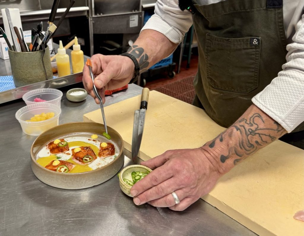 Chef Steven "Chops" Smith adds slices of Serrano pepper onto a plate with tweezers.
