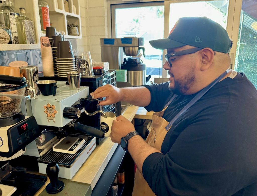 A man froths milk at an espresso machine.