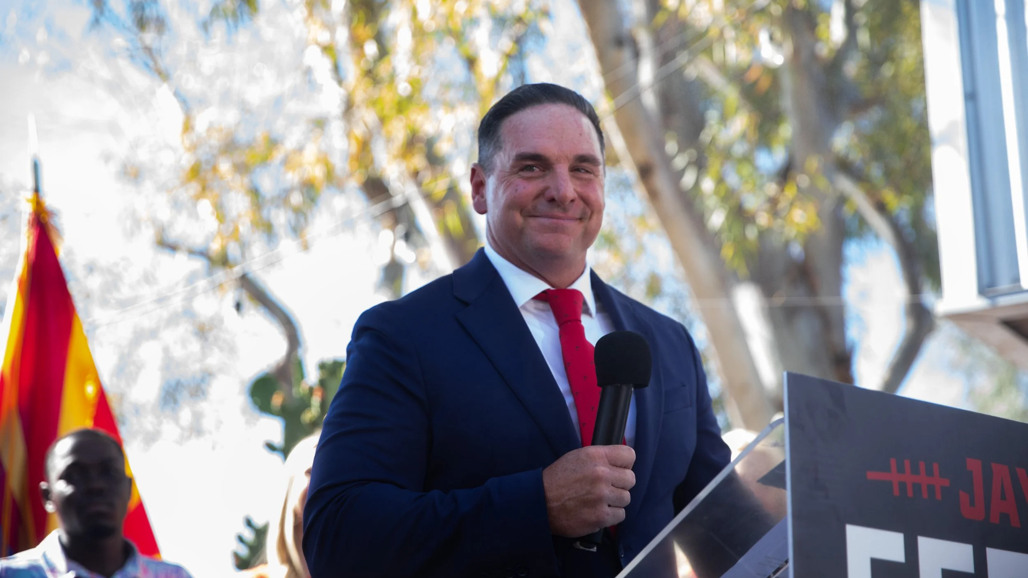 jay feely smiles in a suit while holding a microphone